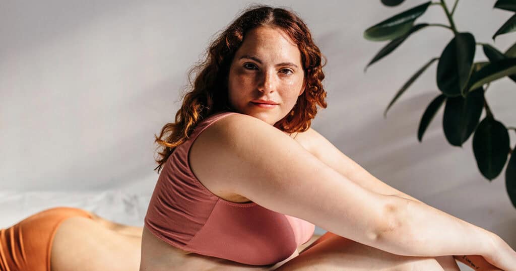 Young woman sitting on bed in underwear, looking at camera