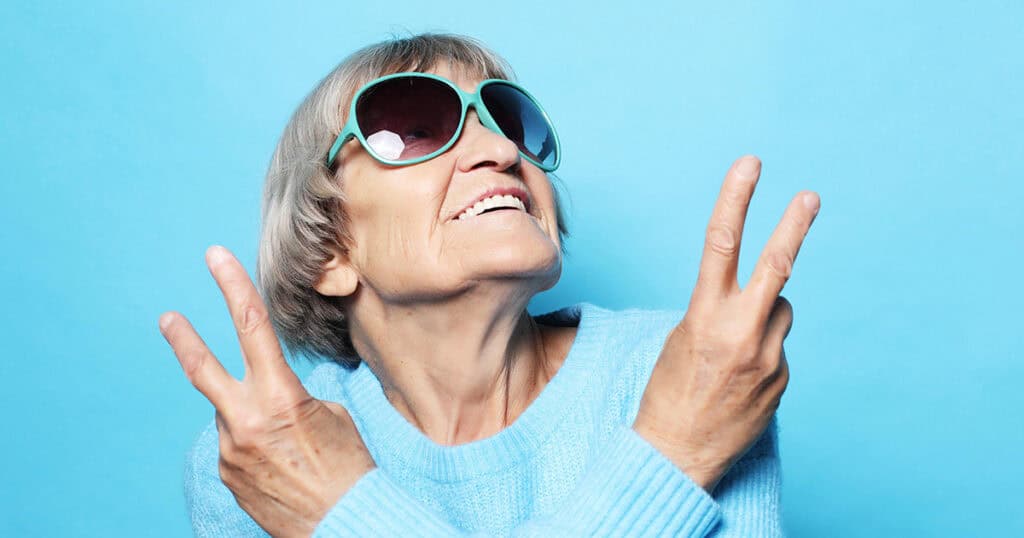 Older white woman in sunglasses and giving peace signs