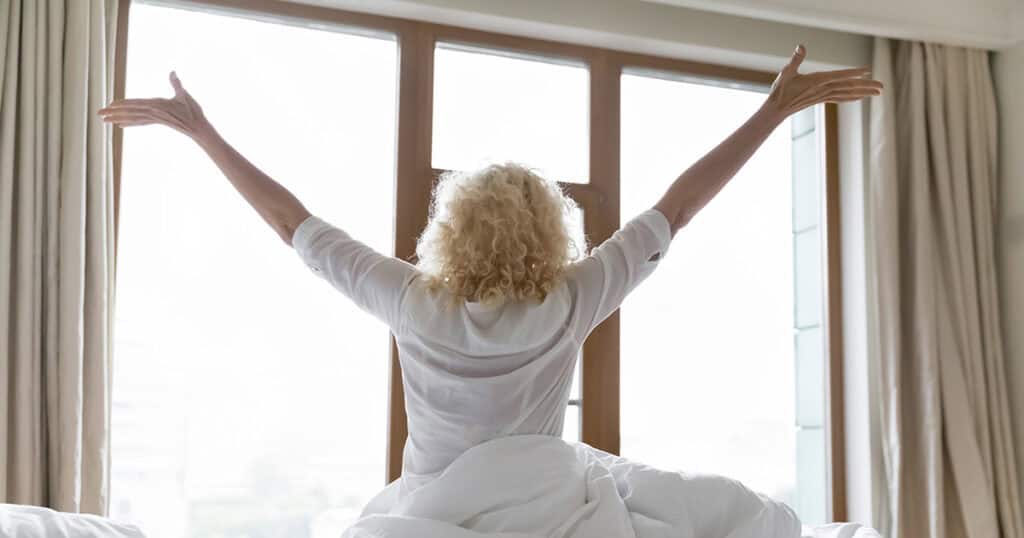 Woman sitting on bed with arms raised joyously