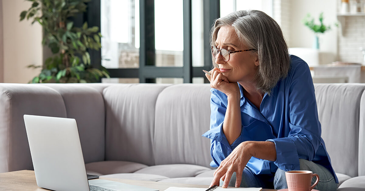 older woman sitting on sofa and researching on laptop computer