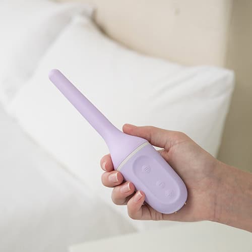 Milli device shown in hand with bed and pillows in background