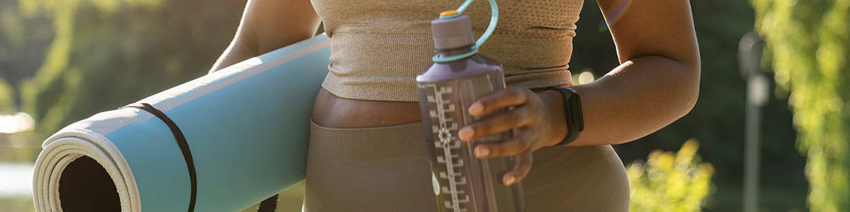 Woman carrying yoga mat under arm and bottle of water in left hand